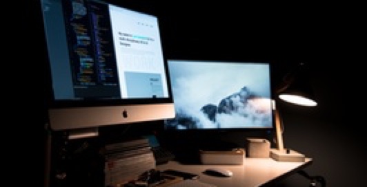 a dimly lit desk with two computer monitors